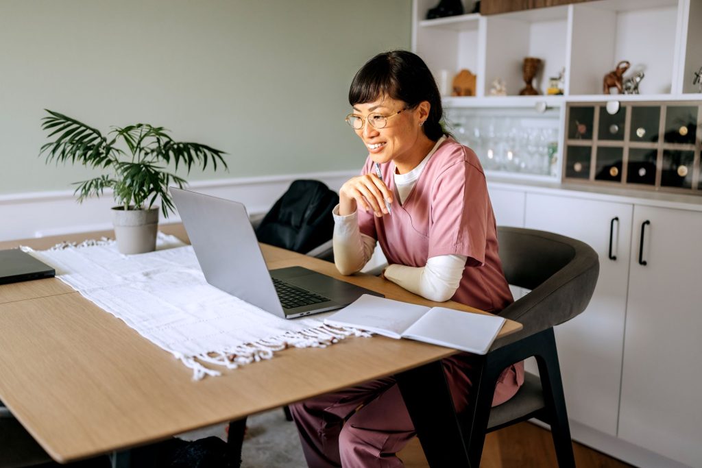 Nurse sitting at table on laptop, undertaking online study